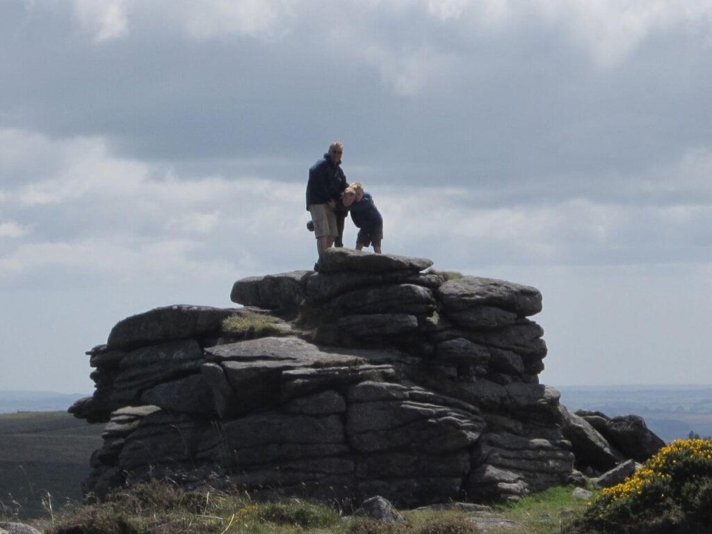 Father and 2 children smiling and laughing having climbed onto the top of a small granite outcrop on Dartmoor in Devon