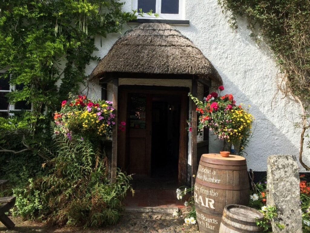 Picturesque thatched Porch entrance to Lustleigh's thatched pub surrounded by colourful flowers and wisteria enticing you in with an open door and warm Dartmoor welcome