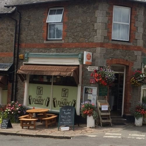 Hanging baskets and flowering pots decorate the outside of Lustleigh's well stocked village shop and Post Office along with seating to enjoy one of the fresh filled baguettes advertised on the chalk board outside the shop