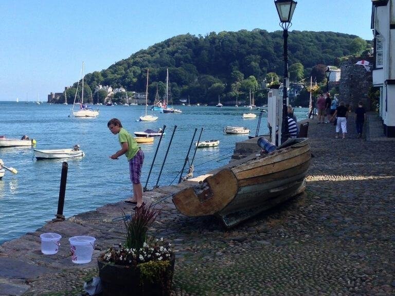 Boy crabbing off Dartmouth's cobblestone quay with small boats all around