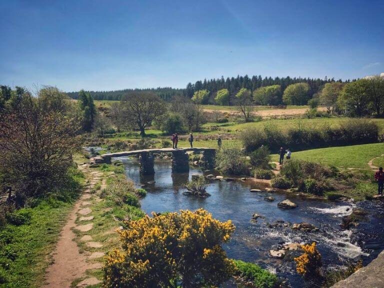 Walkers crossing the ancient clapper bridge at Postbridge on a sunny day