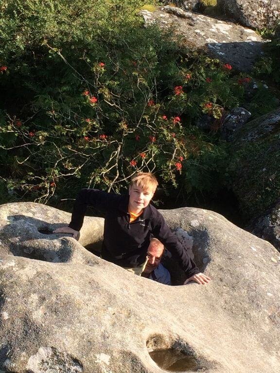 Young boy passing through a hole in a large granite boulder known as the Tolmen Stone