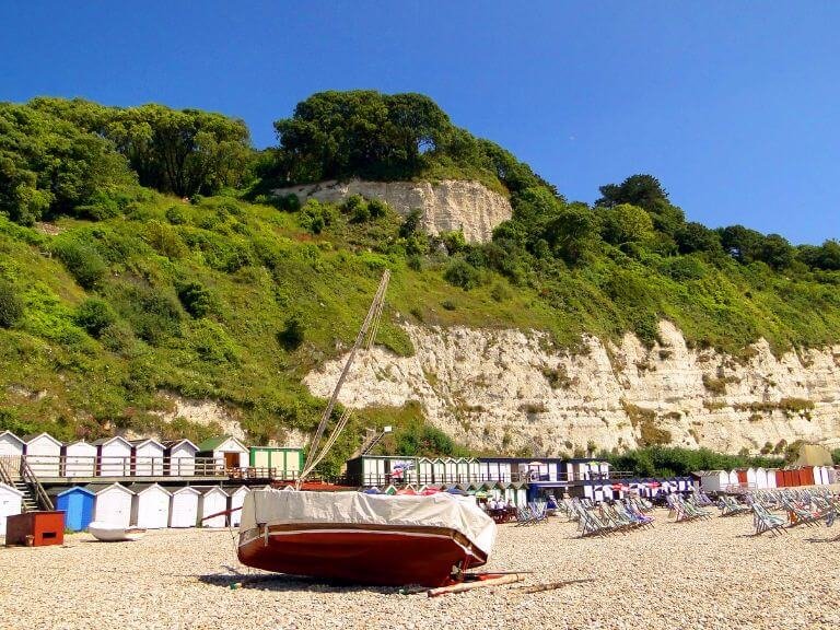 Fishing boat on Beer beach next to deck chairs and beach huts