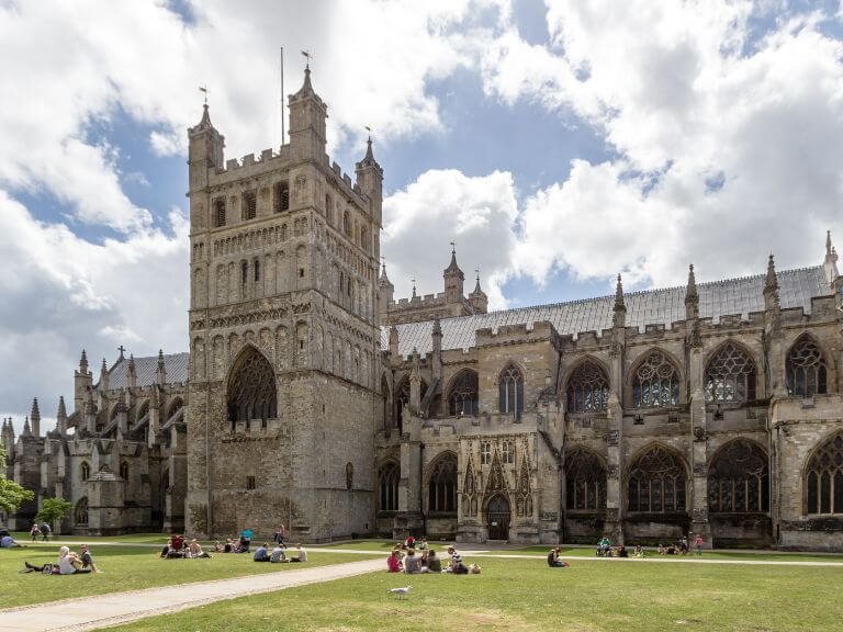 Groups of people sitting on the grass in front of Exeter Cathedral