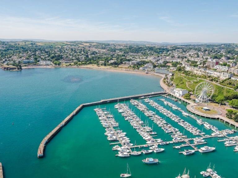 Fleet of yachts moored in Torquay Marina next to long sandy beach with clear blue water