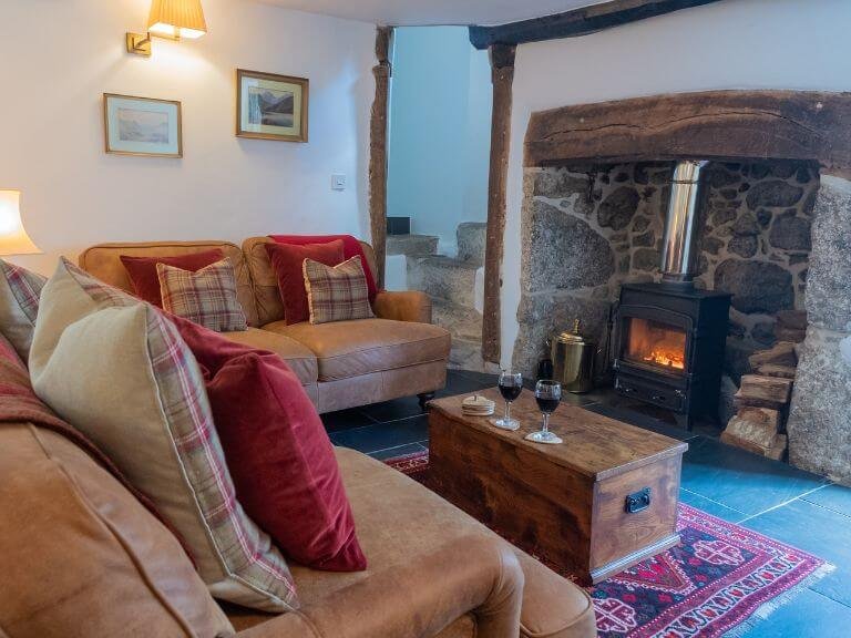 Leather sofa's around a glowing wood burner within inglenook fireplace with glasses of red wine resting upon an antique chest