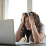 Pretty young lady with head in hands in front of open silver laptop