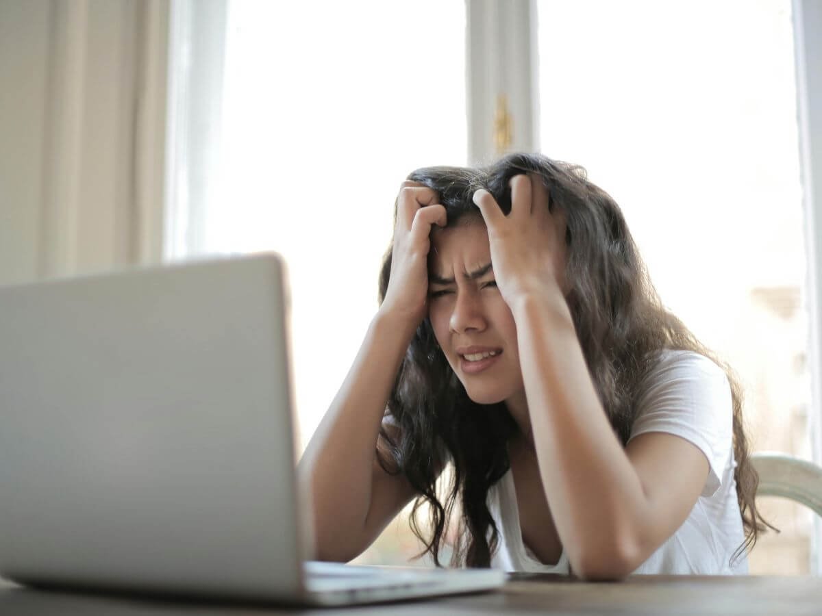 Pretty young lady with head in hands in front of open silver laptop